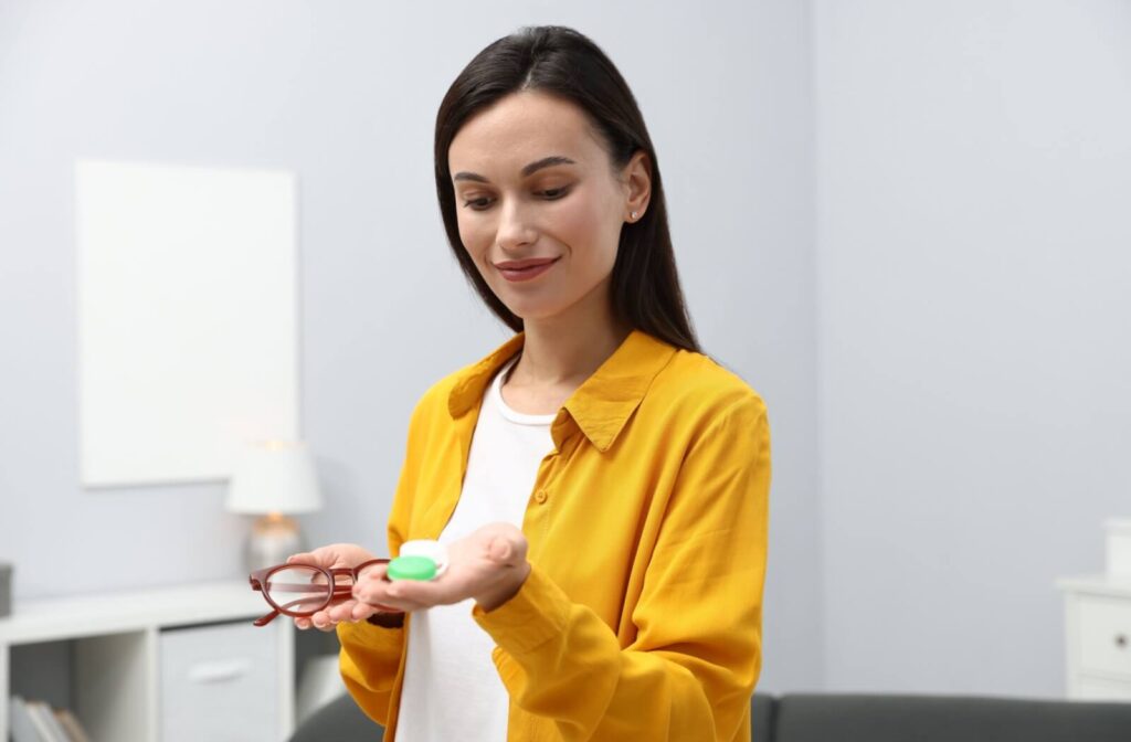 An individual holding a pair of eyeglasses in one hand and a green contact lens case in the other while looking down at them.